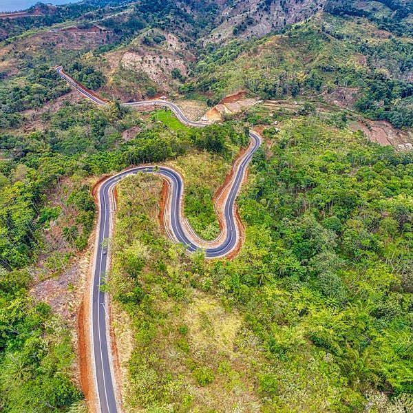An aerial view of a winding road snaking through a hilly, forested landscape.