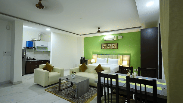 Living and dining area of Lime Tree Hotels & Service Apartment Private Limited featuring a green accent wall, seating, and a dining table.