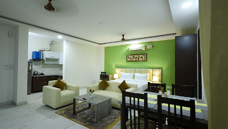 Living and dining area of Lime Tree Hotels & Service Apartment Private Limited featuring a green accent wall, seating, and a dining table.