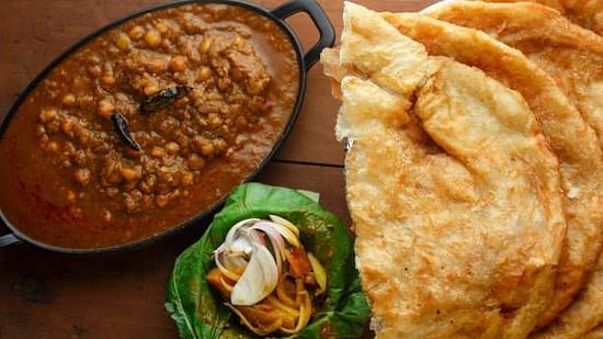 A plate of chole served with large, crispy bhature and sliced onions.