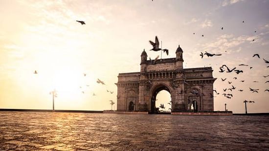 The iconic Gateway of India stands tall by the sea, with birds in flight and golden morning light enhancing the scene.