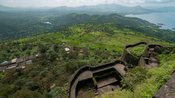 Panoramic view of an ancient fort set amidst dense greenery and overlooking a distant lake.