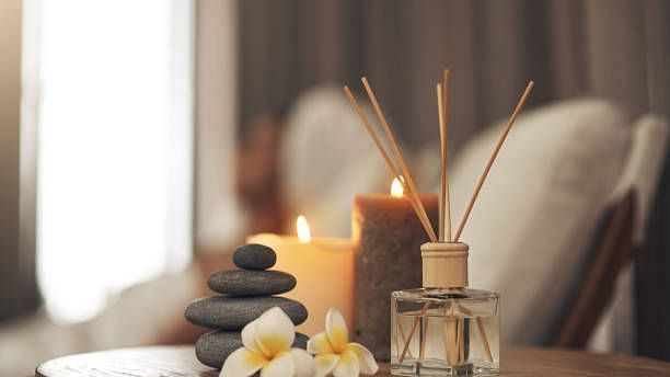 Relaxing spa-like scene with candles, diffuser, stones, and flowers.