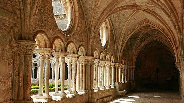 Interior of a historic cloister with arched columns, warm lighting casting long shadows on the narrow pathway.