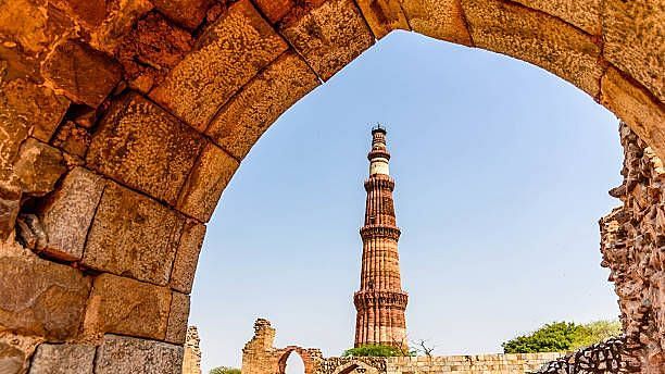 Qutub Minar framed through a stone archway, showcasing the historic Indo-Islamic architecture against a clear blue sky.