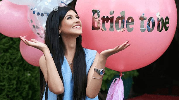 Happy bride-to-be with pink balloon and sash, celebrating her bridal shower with excitement and joy.