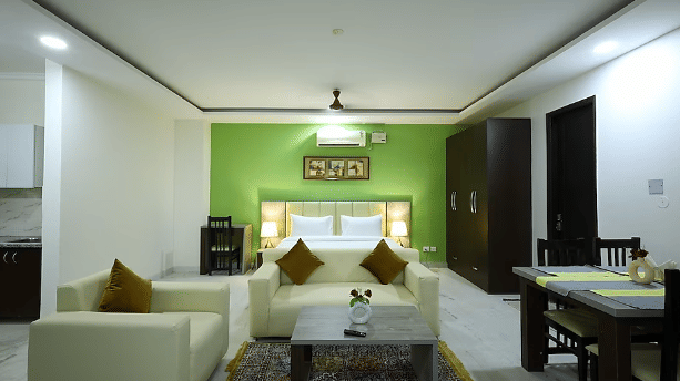 Living and dining area of Lime Tree Hotels & Service Apartment Private Limited featuring a green accent wall, a sofa, and a dining table.