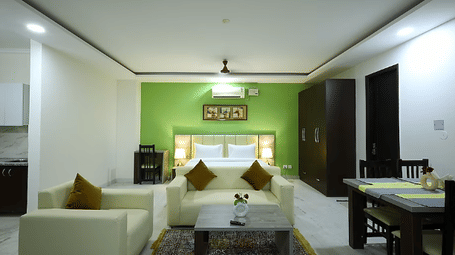 Living and dining area of Lime Tree Hotels & Service Apartment Private Limited featuring a green accent wall, a sofa, and a dining table.