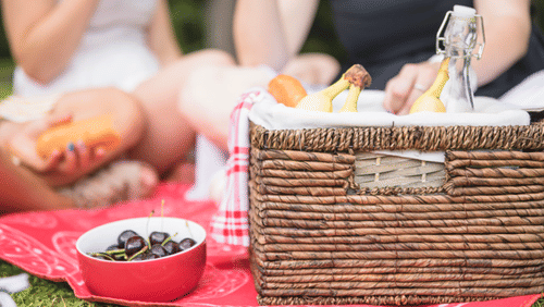 bowl-of-cherry-and-picnic-basket-with-people-in-the-background 23-2147908317