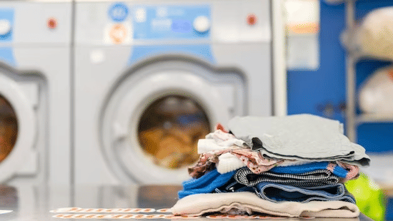 A stack of folded clothes kept on a table with washing machines in the background.