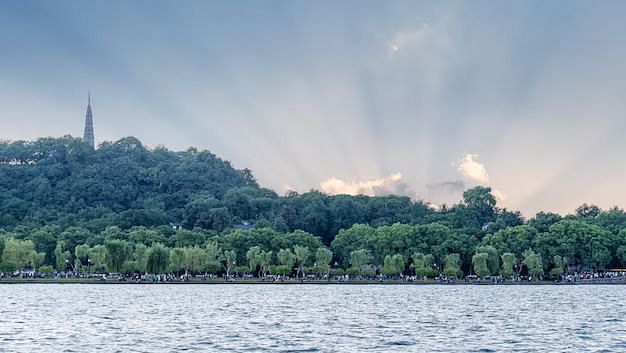 lake in front of forest covered with trees with sun rays shining through the clouds - Chunda Hotels
