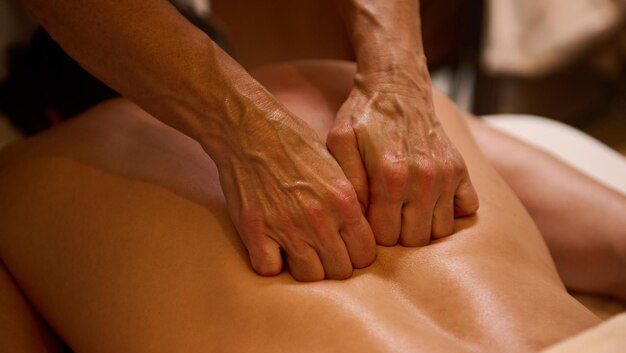 A spa therapist is giving a deep tissue back massage to a person lying face down, using their knuckles.