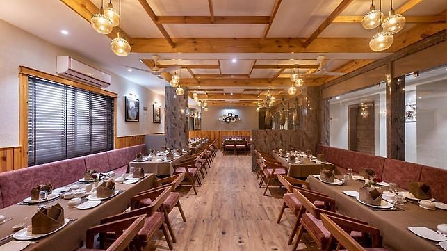A dining area with multiple tables and chairs set for meals along a corridor with a wooden theme at Angel Lords Eco Inn Amreli.