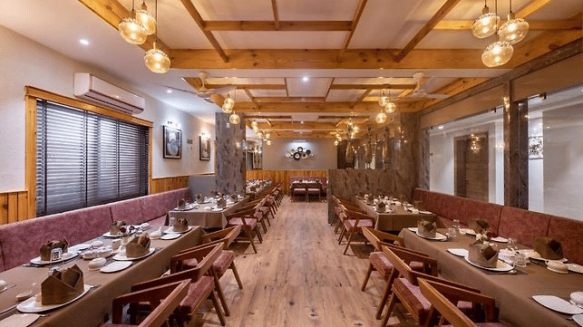 A dining area with multiple tables and chairs set for meals along a corridor with a wooden theme at Angel Lords Eco Inn Amreli.