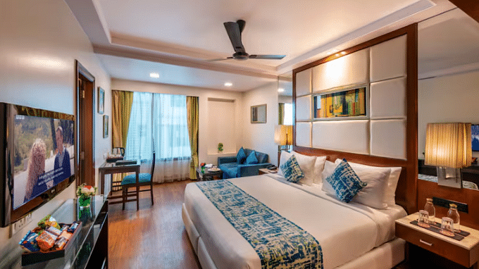 A well-appointed hotel room features a king-sized bed, a seating area with a sofa and table, a work desk, and a television. 