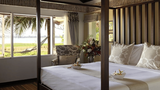 Bedroom in the Waterfront Villa at The Serai Kabini featuring a plush bed next to a seating space by the window with the view of Kabini backwaters