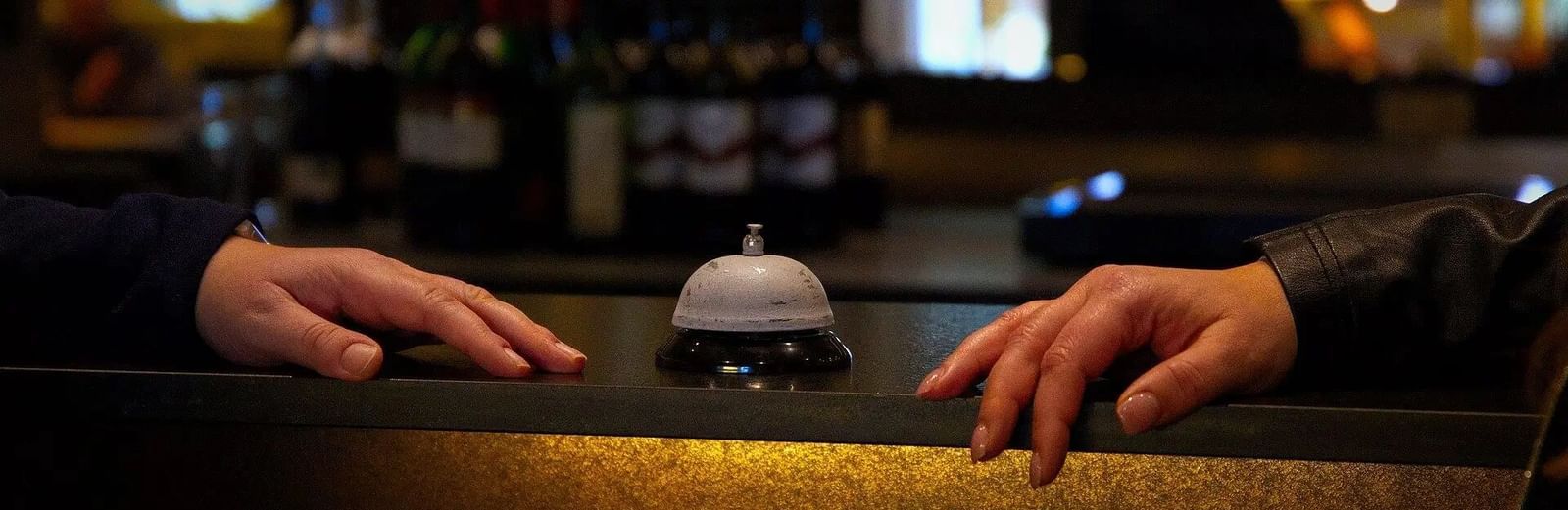 Hands are resting on a bar counter with bottles and glasses visible in the background.