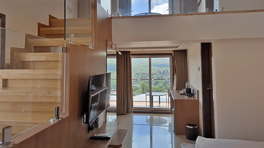 Room with a double bed, television, wooden staircase, and glass railing