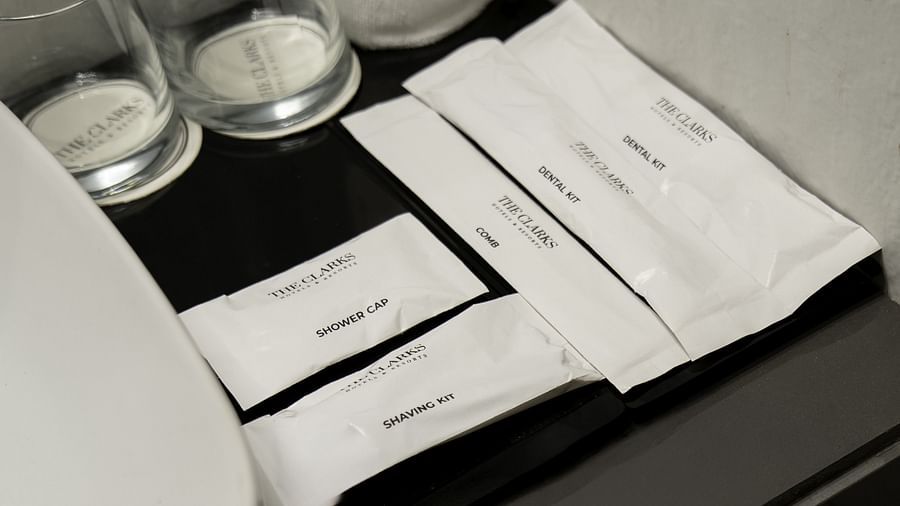 Toiletries from Clarks Inn, Near Kainchi Dham, including a shower cap, shaving kit, comb, and dental kits, arranged on a black surface with drinking glasses.