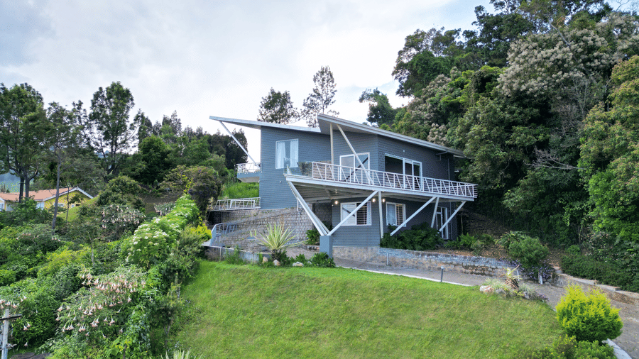 Front view of a contemporary house situated on a grassy hill with trees in the background at Ibex Resorts, Coonoor (Tapas).