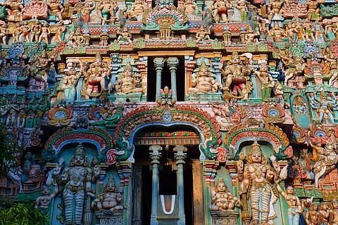 A close-up of a vividly painted temple entrance, densely packed with intricate carvings of Hindu gods, divine beings, and decorative elements, showcasing fine Dravidian craftsmanship.