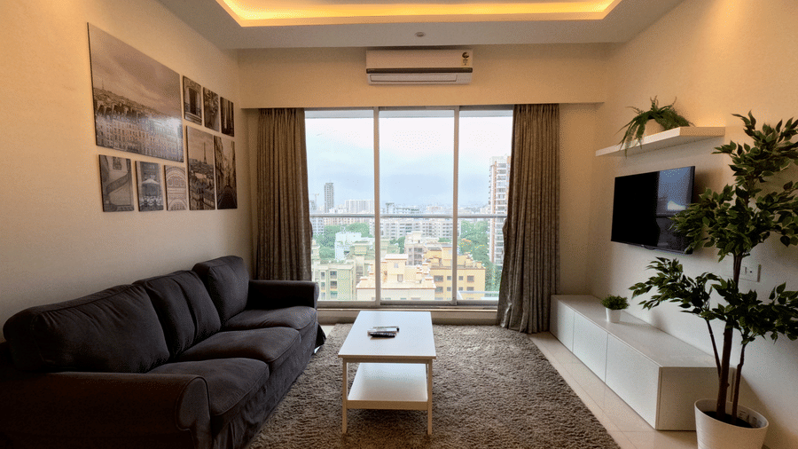 A front view of a living room with a dark grey sofa, coffee table and a TV fitted to the wall