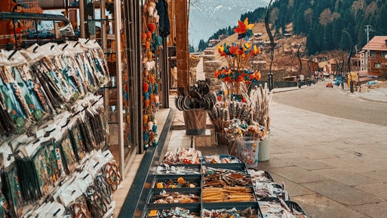 A colourful street market stall displaying vibrant textiles, souvenirs, and trinkets beneath a striped canopy.