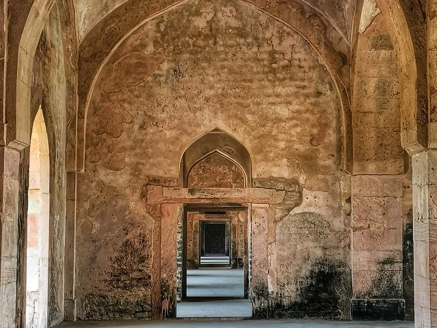 The interior of a historic mosque with intricate arches, ornate carvings, and faded wall paintings.