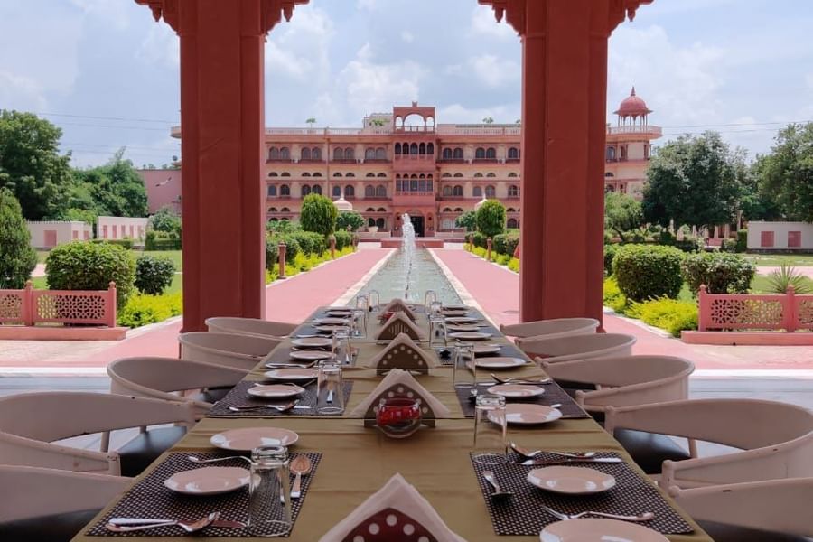 Baradari dining space at Umaid Palace featuring a close up shot of dining table surrounded by chairs. The space provides a view of facade and lawn because of no walls, just pillars and a roof.