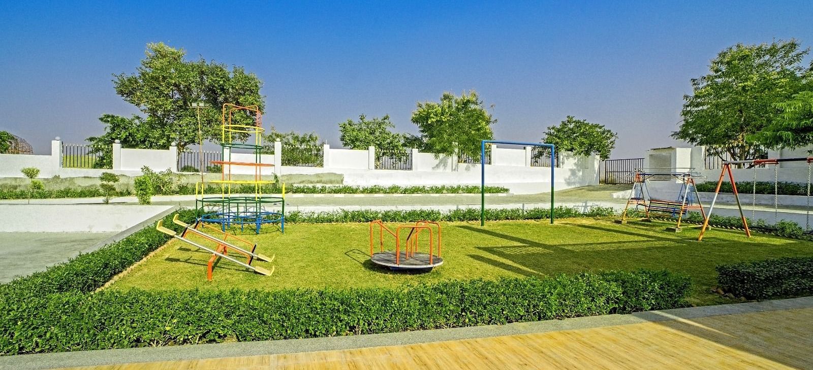 Children’s playground at Grassfield Riveria Resort, Jaipur, featuring swings, a roundabout, and lush greenery under a clear blue sky.