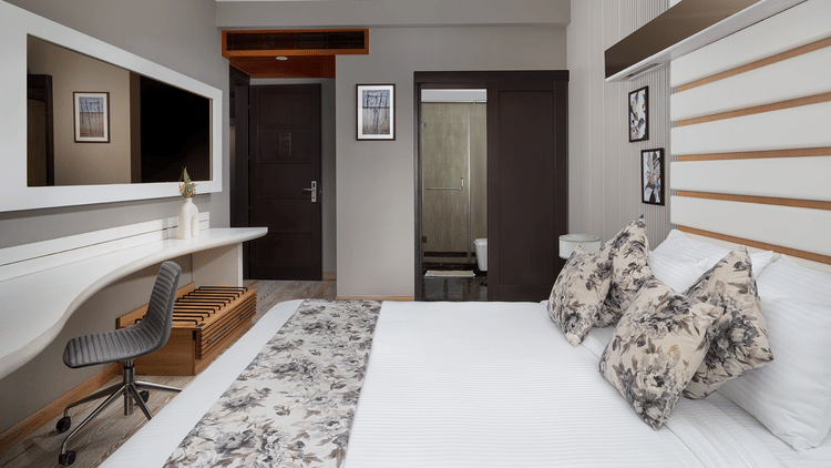 A contemporary bedroom at The Atara, Gurugram featuring a comfortable bed, a functional desk setup, and a wall-mounted television