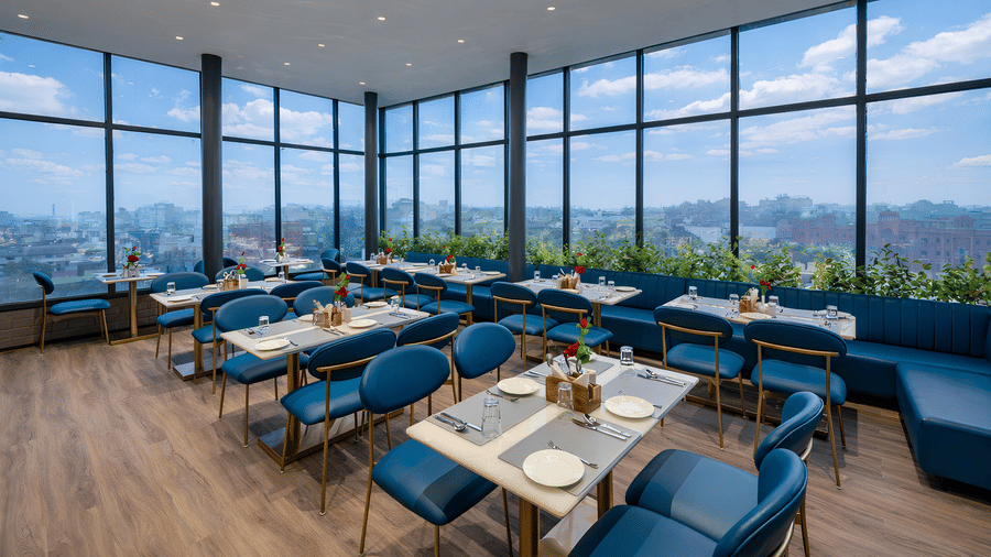 A dining area with multiple tables, chairs, large glass windows, and a view of the outdoors at DLS Hotels Amritsar.
