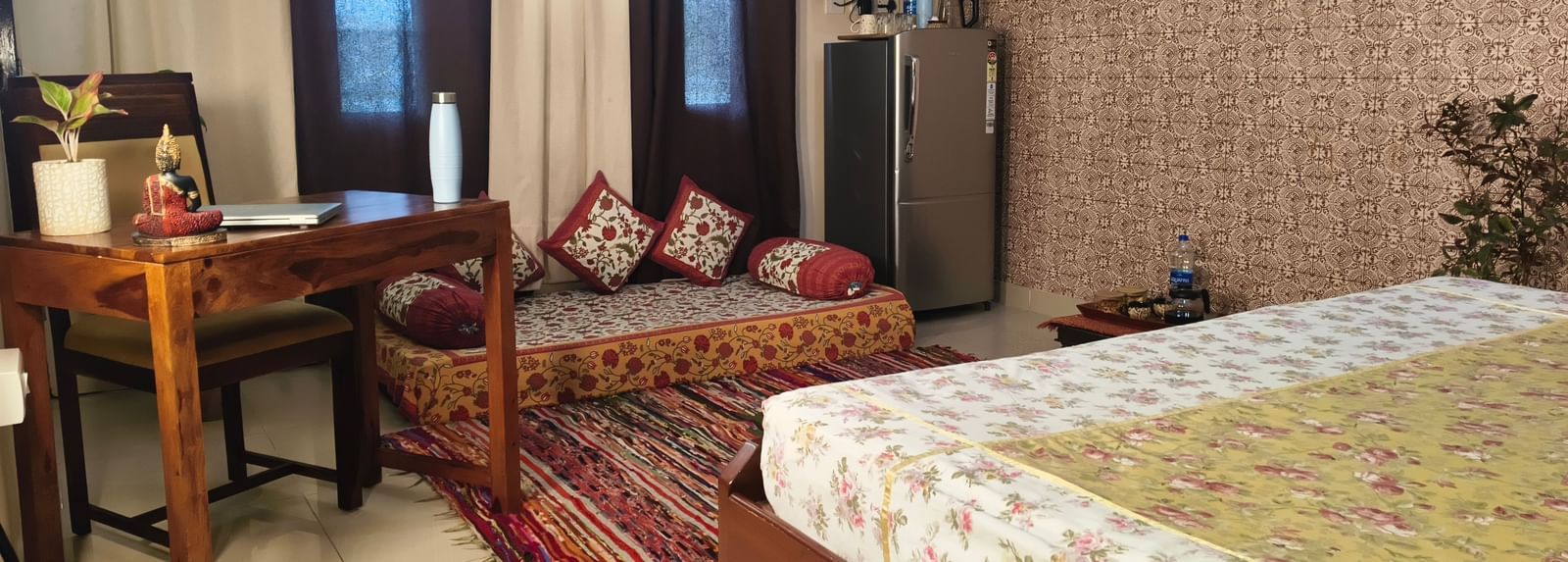 A bedroom with a bed, wooden desk, cushions arranged on divan seating and wall decor at Jaypore360 Homestay in Jaipur.