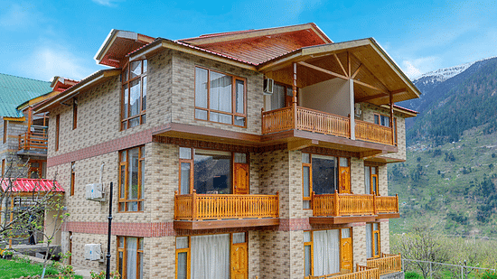 Facade of Clarks Inn Suites in Manali with lawn surrounding the bulding under clear blue sky with mountains in the background