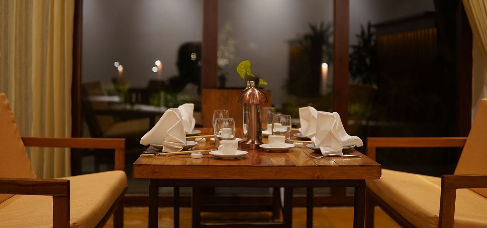 Seating arrangement at Asian Table at Saraca Resort & Spa Corbett with a wooden theme and large windows at night