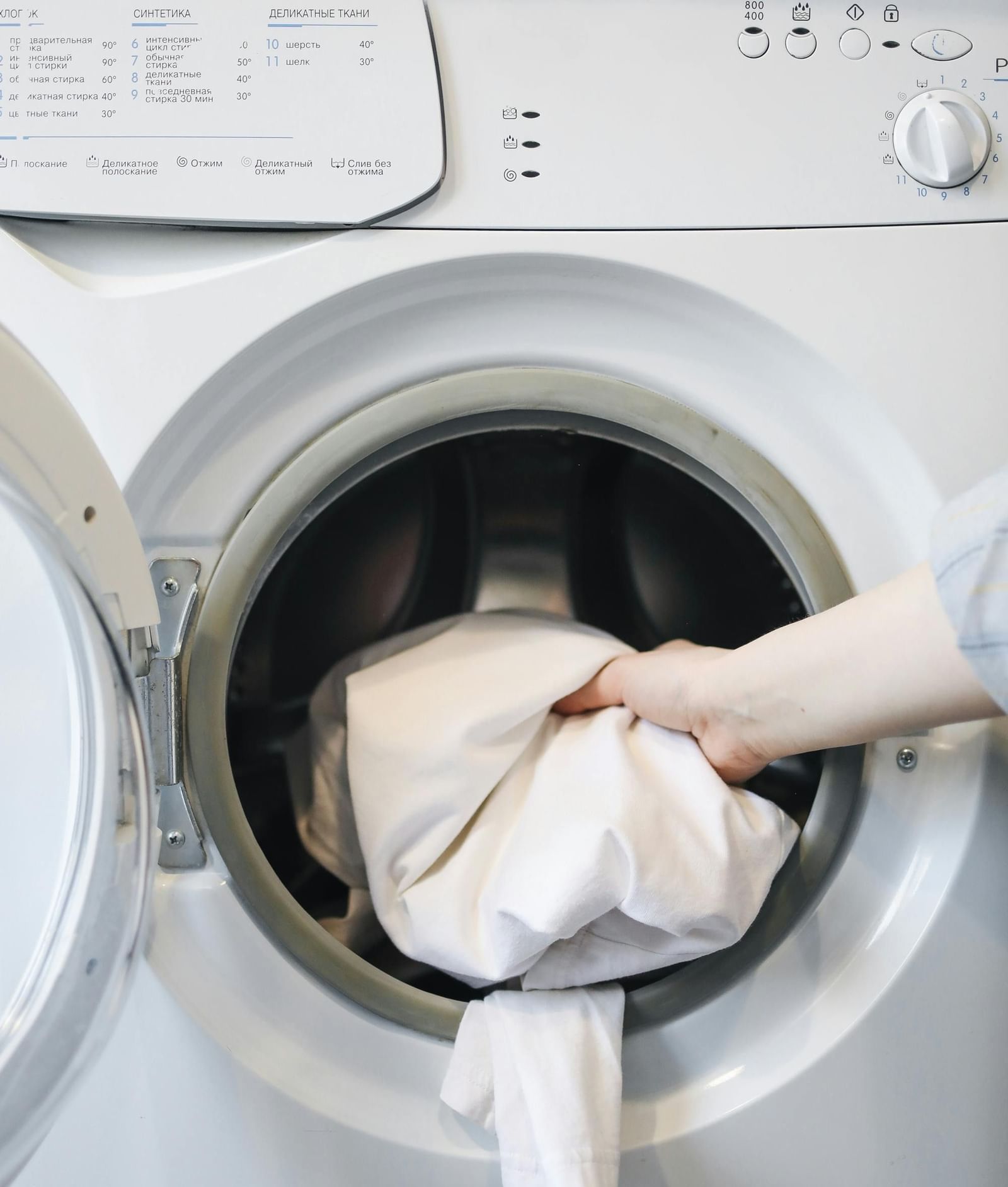 A person loading laundry into a front-loading washing machine.