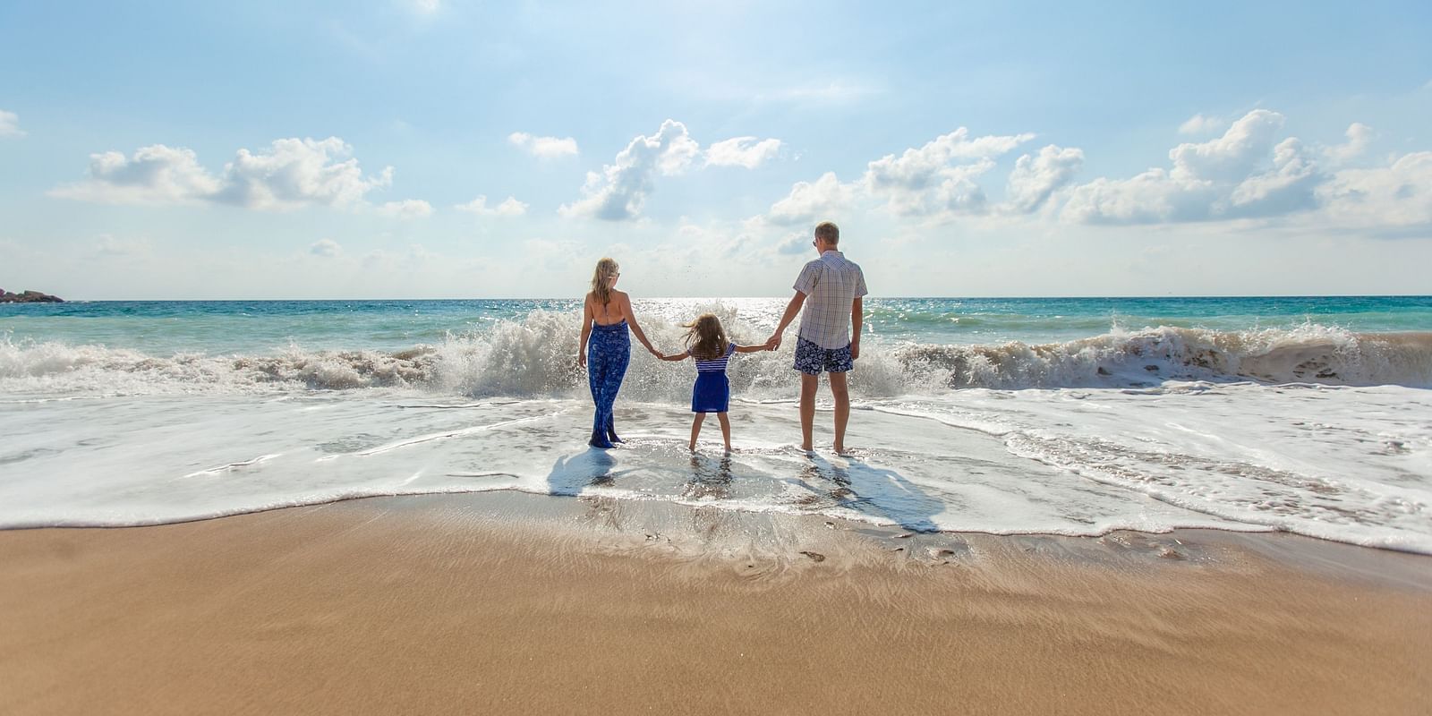A family holding hands and walking into the waves, enjoying a sunny day at the beach together.