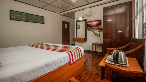 An image of bedroom featuring, a dressing table, TV, chair, table with a tea and coffee maker, and a fan - Central Hill Resort, Gangtok
