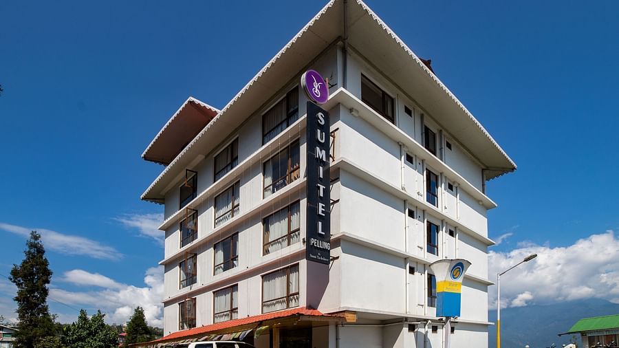 The exterior of a Sumitel hotel building with balconies, clear blue sky, and a few parked vehicles.