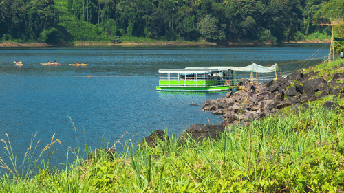 Lush green mountains rise behind a calm lake under a bright blue sky.