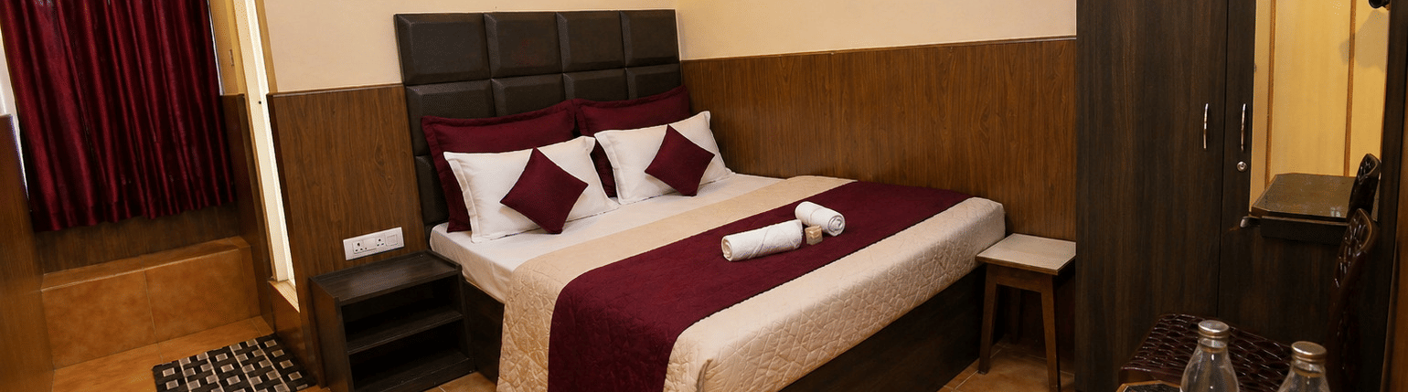 A neatly-made bed with towels, a tall wooden wardrobe, and a small bedside table in the Deluxe Double Room With Extra Cot at BN Tourist Home, Ooty.