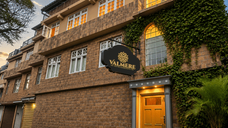 Exterior facade of Valmere Thistle Boutique Hotel, Darjeeling at dusk with a stone facade, ivy-covered wall, hanging signboard, and yellow door.