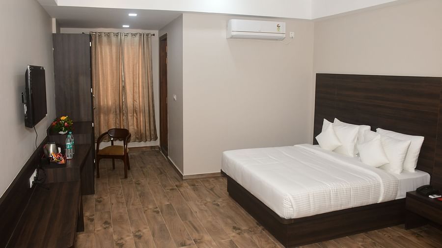 A bedroom features a double bed, dark wooden furniture, and neutral-toned walls - Kankidham Lords Inn