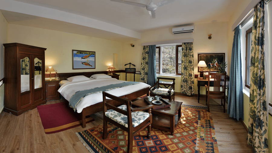 Refined bedroom with polished wooden flooring large bed seating corner and ample daylight ensuring a serene stay at Neemrana’s Glasshouse on The Ganges with a balance of comfort and elegance