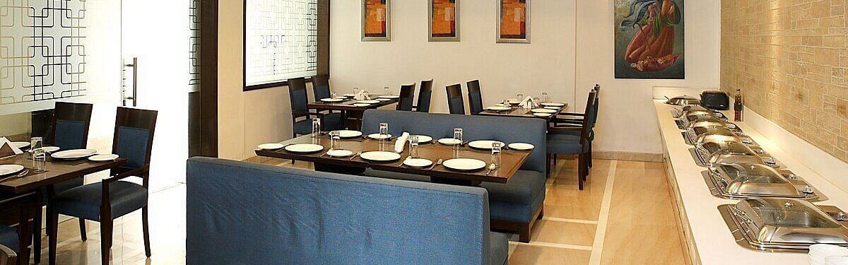 Tables and chairs neatly arranged with cutlery set on the table at Café Inde, Inde Signature Tower, Gurgaon