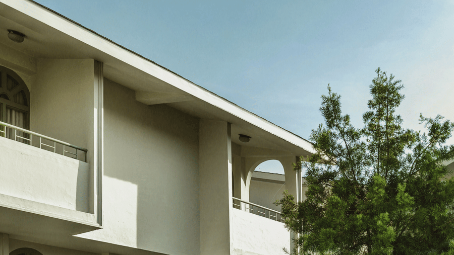 Front view of a resort building at Mango Hill Shola, Ooty, featuring a bench placed near the entrance and surrounded by natural foliage.