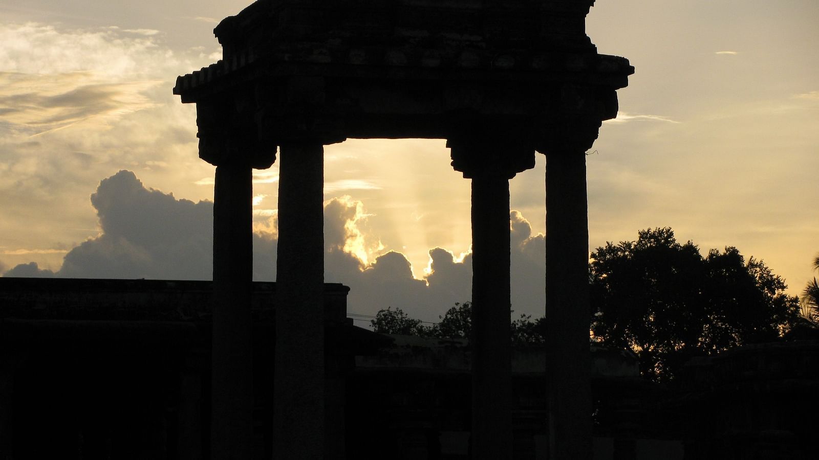 An overview of ancient columns in Belur with the sun's rays behind the clouds in the background.
