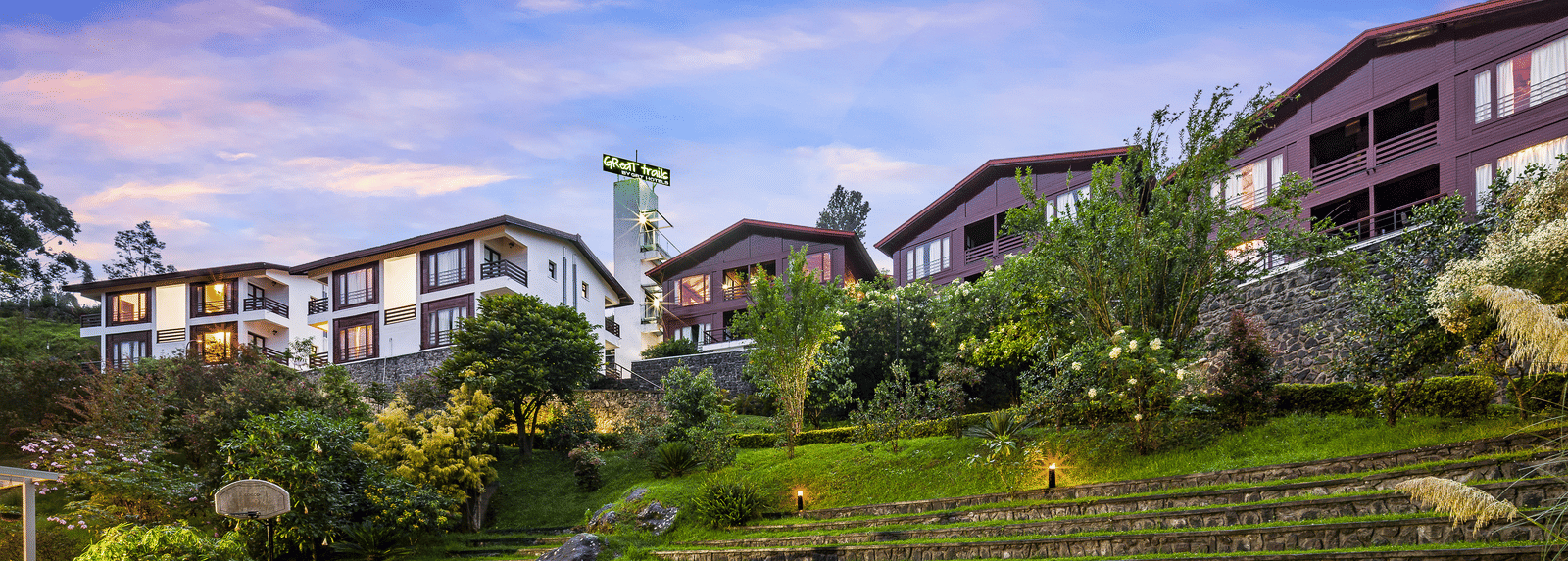 Exterior view of the hotel with lush greenery with the hotel buildings in the background - GReaT Trails Kodaikanal By GRT Hotels