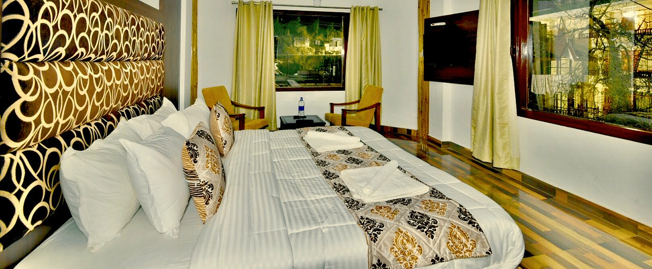 An image of the king size bed at the resort with expansive windows around | DLS Kapoor Resort Manali