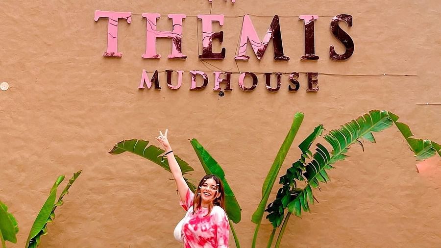 a woman with her luggage standing in front of Themis Mudhouse - A Nature's Retreat Resort & Wellness